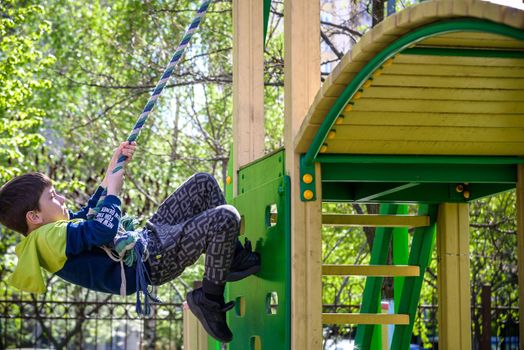 Teenager boy climbing at kid playground outdoor. The climber trains simulator on the street. Healthy leisure for children concept.