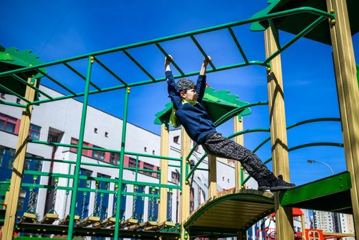 Teenager boy climbing at kid playground outdoor. The climber trains simulator on the street. Healthy leisure for children concept.