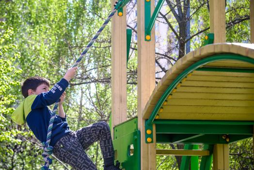 Teenager boy climbing at kid playground outdoor. The climber trains simulator on the street. Healthy leisure for children concept.