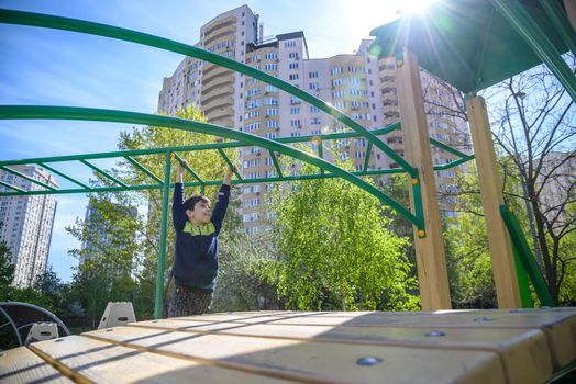 Teenager boy climbing at kid playground outdoor. The climber trains simulator on the street. Healthy leisure for children concept.