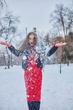 a young happy woman is having fun in a winter park, throwing snow, it is cold in her hands, the emissions are off scale