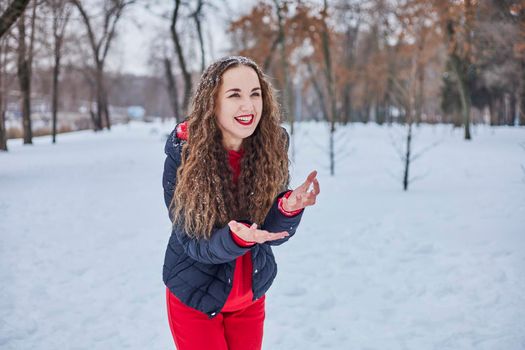 a young happy woman is having fun in a winter park, throwing snow, it is cold in her hands, the emissions are off scale