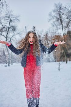 a young happy woman is having fun in a winter park, throwing snow, it is cold in her hands, the emissions are off scale