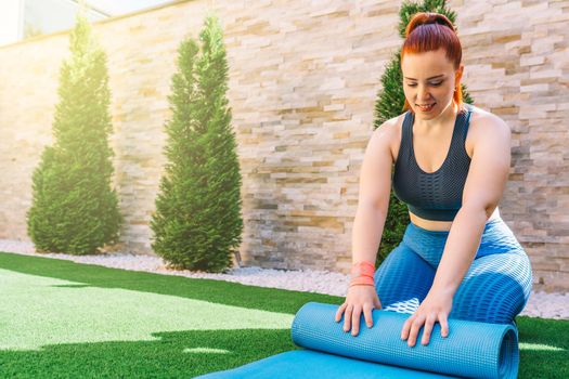 Attractive young fitness girl exercising outdoors in the garden of her home, preparing for stretching exercises. health and wellness concept.natural light in the garden.