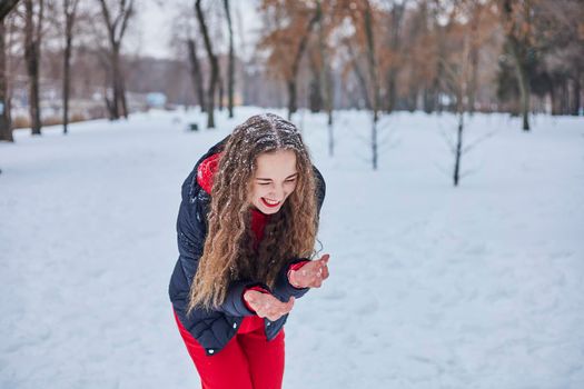 a young happy woman is having fun in a winter park, throwing snow, it is cold in her hands, the emissions are off scale