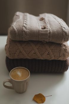 cozy home atmosphere and still life with a cup, candle and sweaters on a table.