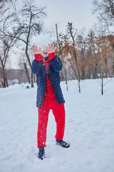 a young happy man is having fun in a winter park, throwing snow, it is cold in his hands, the emissions are off scale