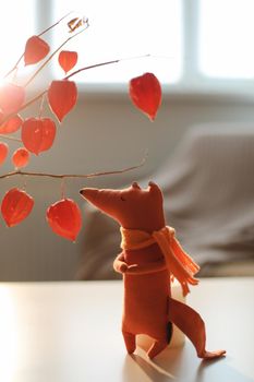 autumn still life with a toy fox, flowers, twigs of red physalis in a vase in a cozy home interior.