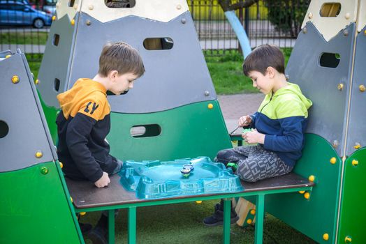 Two Boys playing with modern spin top outdoors. Entertainment game for children. Top, triggered by a trigger. Kids having a tournament on arena or battle field.