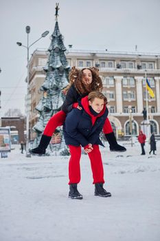 young family guy and girl spend the day in the park on a snowy day. Emotional young couple having fun while walking in the winter city, a lively man hugs his laughing beautiful woman