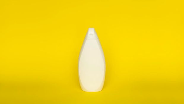 White plastic shampoo bottle isolated on yellow background. Skin care lotion. Bathing essential product. Shampoo bottle. Bath and body lotion. Fine liquid hand wash