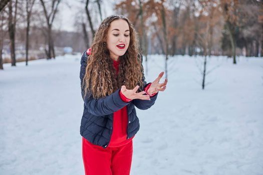 a young happy woman is having fun in a winter park, throwing snow, it is cold in her hands, the emissions are off scale