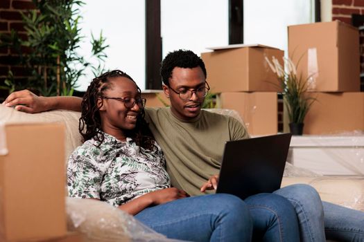 African american partners finding furniture on online website, shopping on laptop to decorate rented flat. Buying decorations on internet browser after moving in new home property.