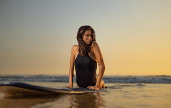 Surf girl with long hair go to surfing. Woman holding surfboard on a beach at sunset or sunrise. Surfer and ocean.