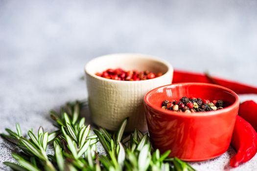 Bowl with pepper spice mix, rosemary herb and red hot chilli pepper vegetable on grey concrete table