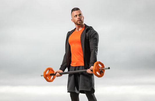 Bodybuilder in orange sportswear doing barbell exercises for biceps in the outdoors gym. Powerful fitness workout