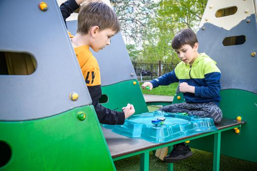 Two Boys playing with modern spin top outdoors. Entertainment game for children. Top, triggered by a trigger. Kids having a tournament on arena or battle field.