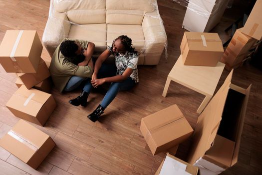 Cheerful homeowners sitting on apartment floor after moving in and relocating in new property. Feeling relaxed and happy about starting new beginnings, celebrating life event. Top view of.