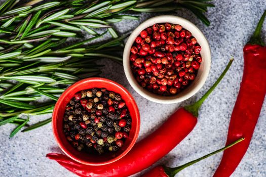 Bowl with pepper spice mix, rosemary herb and red hot chilli pepper vegetable on grey concrete table