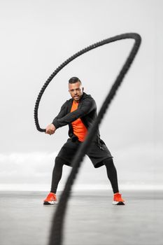 Athletic man with a battle rope doing sports exercises on the ocean.