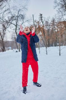 a young happy man is having fun in a winter park, throwing snow, it is cold in his hands, the emissions are off scale