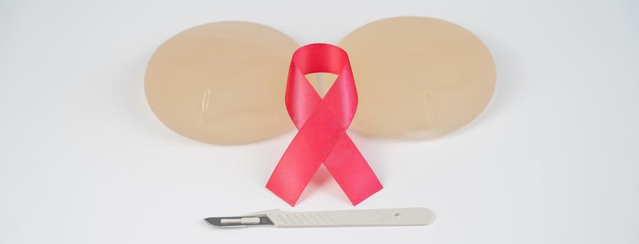 Breast silicone implants, pink tape and a disposable scalpel on a white background