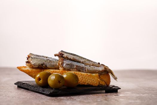 tapa of sardines with tomato and olives on black slate and white background typical Spanish