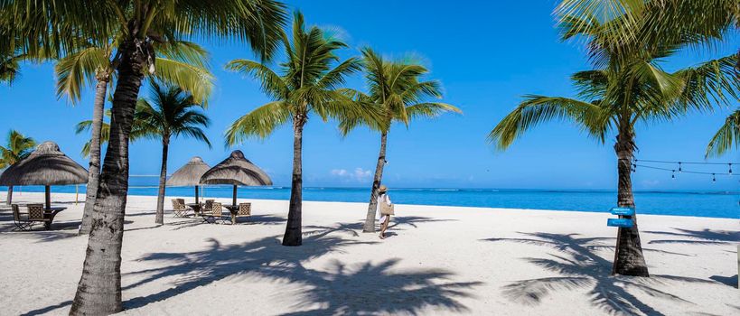 Le Morne beach Mauritius Tropical beach with palm trees and white sand blue ocean and beach beds with umbrellas, sun chairs, and parasols under a palm tree at a tropical beach. Mauritius Le Morne beach
