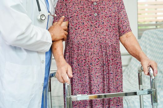 Doctor help Asian elderly woman disability patient walk with walker in nursing hospital, medical concept.