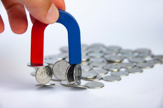 Hand holding magnet attracting silver coins with white cover background. Business and law of attraction concept
