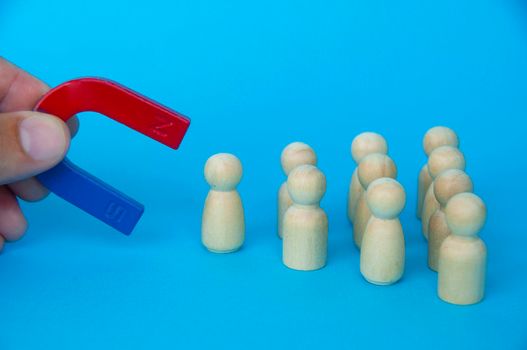 Hand holding magnet attracting wooden doll figures on blue background. Business and law of attraction concept