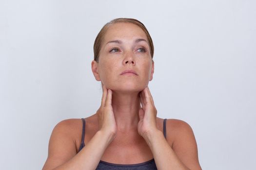 Portrait of caucasian middle aged woman of 40s examining lymph nodes on neck to diagnosing lymphoma, hypothyroidism, tonsillitis on white background looking up
