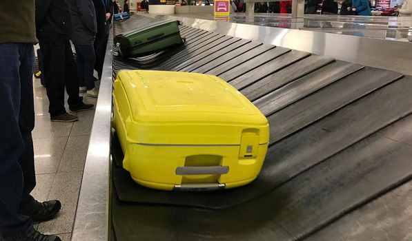 Lisbon, Portugal - March 3, 2017 - Yellow suitcase on a conveyor belt in Lisbon airport (Humberto Delgado Airport). People are waiting to reclaim their luggage