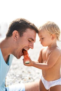 Little daughter feeding dad with watermelon on the beach. High quality photo
