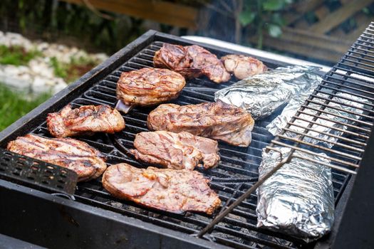 Pieces of fresh meat and fish in foil are laid out on a grill grate. Barbecue cooking. Selective focus.