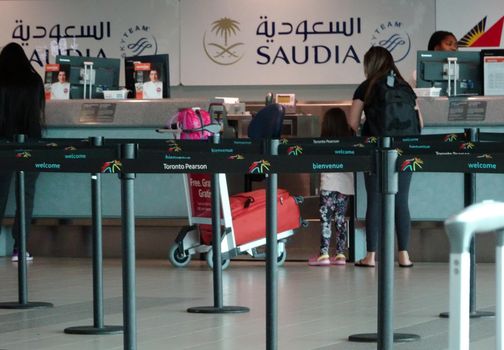 Toronto, Ontario, Canada - Oct 26 2016 Toronto Pearson YYZ Airport A woman and her daughter are checking in on a counter for Saudi Arabian Airlines. She has a huge red suitcase on a trolley