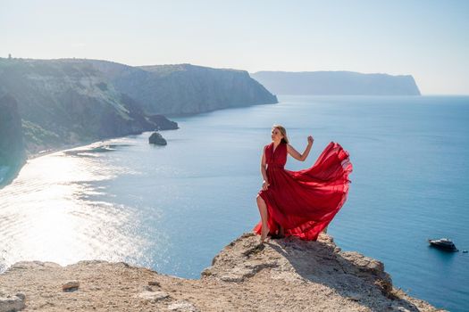 A woman in a red flying dress fluttering in the wind, against the backdrop of the sea