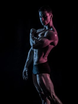 Handsome young bodybuilder doing classic bodybuilding pose, looking away, on greenish background, halffigure shot