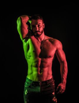 Shirtless muscular male bodybuilder in studio shot on black, with dramatic colorful lighting