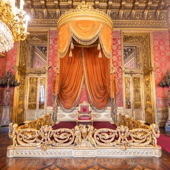 Turin, Italy - Circa August 2021: old throne room interior with chair in luxury palace. Red and gold antique Baroque style - Savoia Royal Palace