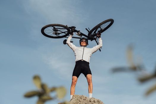 Professional Male Cyclist Raising Hands with Bicycle while Standing on the Top of Hill, Sky on Background