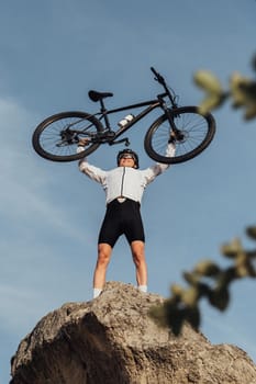 Professional Male Cyclist Raising Hands with Bicycle while Standing on the Top of Hill, Sky on Background