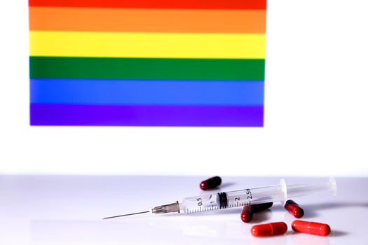 Six Red capsules, syringe and rainbow flag in the background