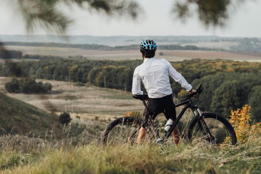 Rear view on Professional Cyclist Leans on His Bike and Enjoys View During Journey