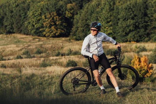 Professional Male Cyclist Leans on Bike and Adult Man Enjoying Rest During His Ride on Bicycle