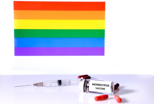 Six Red capsules, syringe and vial and rainbow flag in the background
