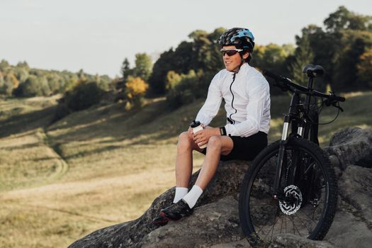 Handsome Professional Male Cyclist Sitting with Mountain Bike on Rock, Adult Man Enjoying His Extreme Hobby with Panoramic View