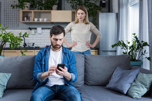 Conflict, young couple, family, man and woman. An angry woman shouts at a man who constantly uses and plays on the phone, does not pay attention