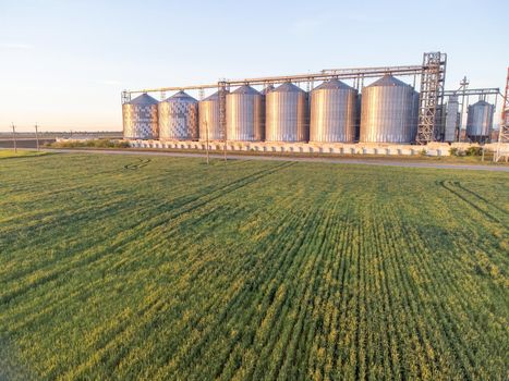 Grain elevator. Metal grain elevator in agricultural zone. Agriculture storage for harvest. Grain silos on green nature background. Exterior of agricultural factory