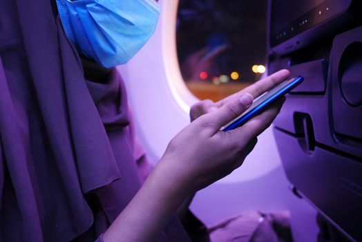 women with a face mask using smart phone sitting on airplane seats in the cabin,